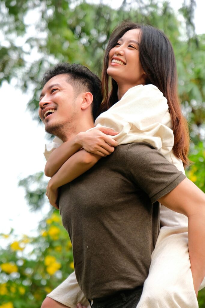 Happy couple enjoys a playful piggyback ride in a sunny outdoor park.